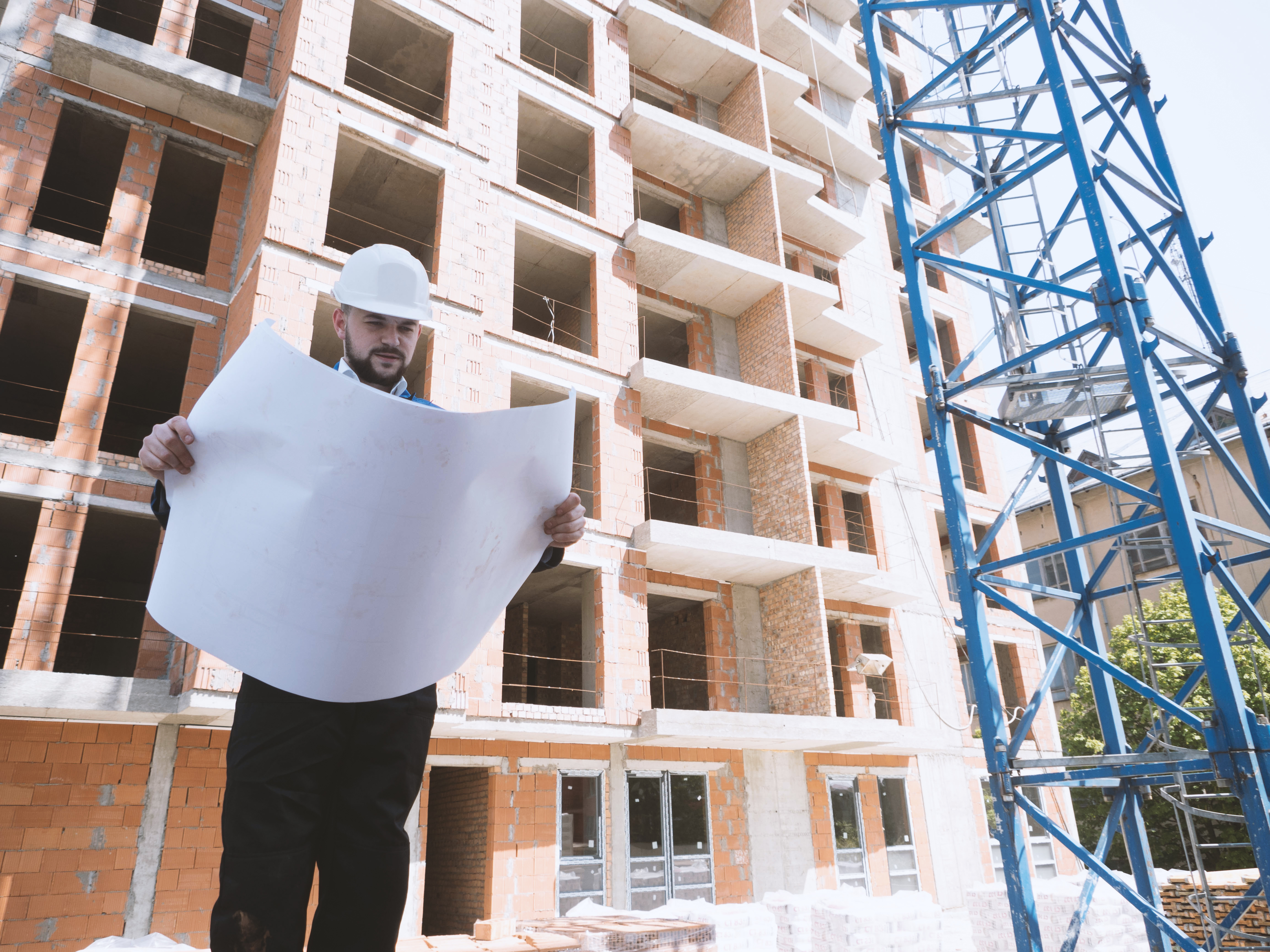 A man holds blueprints in front of a construction site